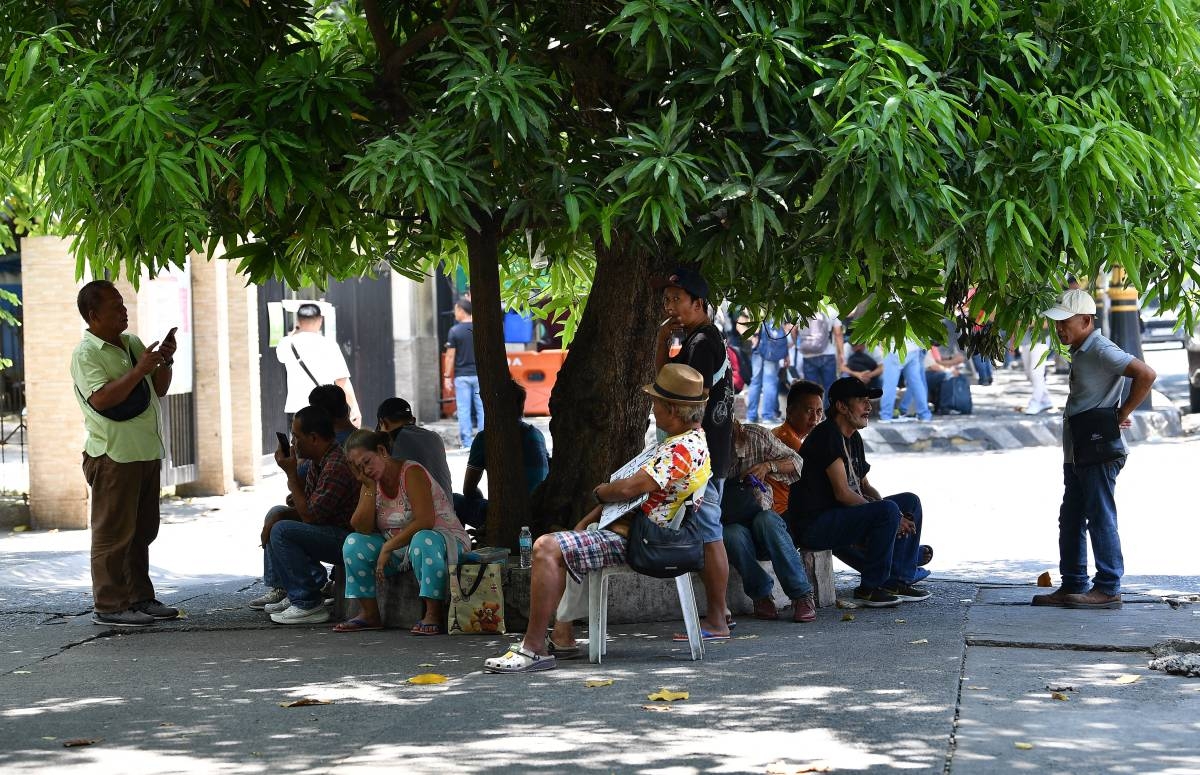 People take shelter under a tree along a road in Manila on April 24, 2024, as extreme heat affected the country. Extreme heat scorched the Philippines on April 24, forcing schools in some areas to suspend in-person classes and prompting warnings for people to limit the amount of time spent outdoors. Ted ALJIBE / AFP