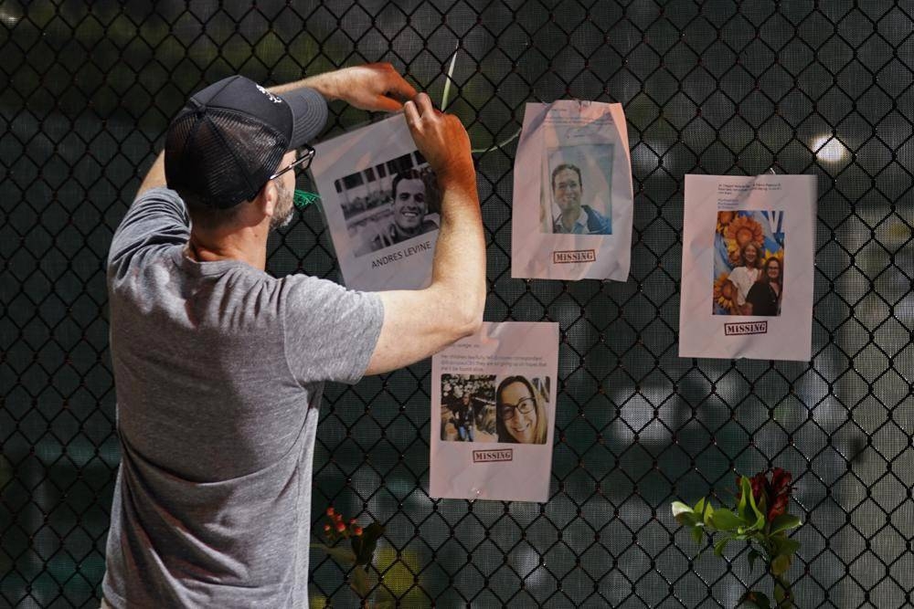 A man hangs a photo on a fence of someone missing near the site of an oceanfront condo building that partially collapsed in Surfside, Fla., Friday, June 25, 2021. AP PHOTO