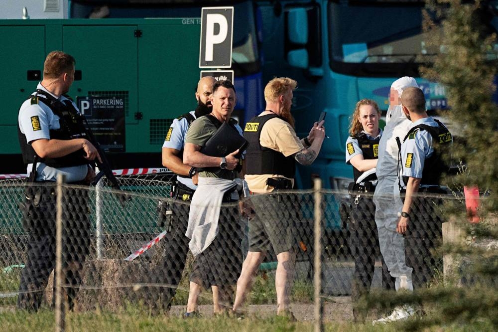 A policeman takes a picture of a man detained and believed to be the suspect (2ndR), at the scene of the Fields shopping center in Copenhagen, Denmark, on July 3, 2022, following a shooting. AFP PHOTO