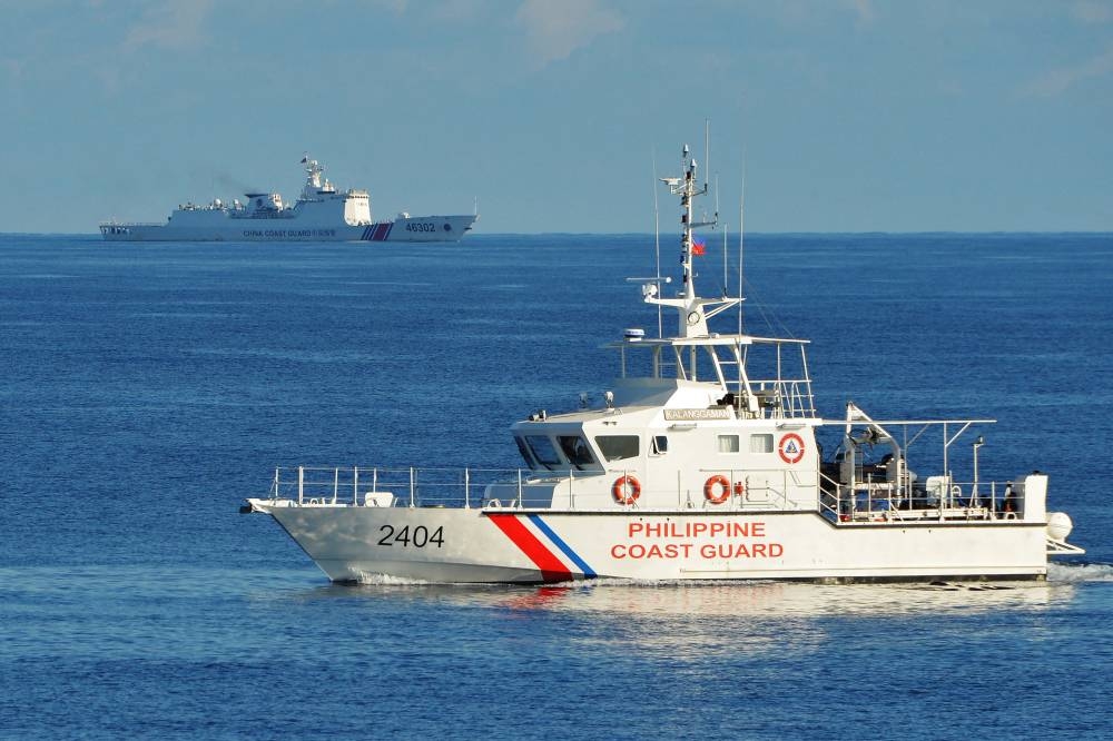 This file photo taken on May 14, 2019 shows a Philippines' coast guard ship (R) sailing past a Chinese coast guard ship during a joint search and rescue exercise between the Philippines and US coast guards near Scarborough Shoal in the South China Sea. - The Scarborough Shoal fishing ground, tapped by generations of Filipino fishermen, is one of many potential flashpoints for military conflict over the South China Sea. China and Taiwan both claim sovereignty over almost the entire sea, while the Philippines, Vietnam, Malaysia and Brunei have competing claims to parts of it. (Photo by Ted ALJIBE / AFP)