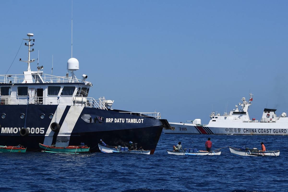 This photo taken on February 15, 2024 shows Filipino fishermen aboard their wooden boats queueing for free fuel beside the Philippine Bureau of Fisheries and Aquatic Resources (BFAR) ship BRP Datu Tamblot (L) as a Chinese coast guard ship (background R) monitors near the China-controlled Scarborough Shoal, in disputed waters of the South China Sea. The Philippines on February 17 accused Chinese coast guard vessels of 