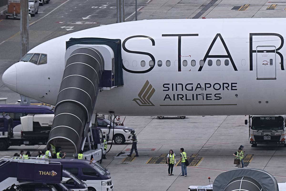 Officials gather around the Singapore Airlines Boeing 777-300ER airplane, which was headed to Singapore from London before making an emergency landing in Bangkok due to severe turbulence, as it is parked on the tarmac at Suvarnabhumi International Airport in Bangkok on May 22, 2024. A 73-year-old British man died and more than 70 people were injured on May 21 in what passengers described as a terrifying scene aboard Singapore Airlines flight SQ321 that hit severe turbulence, triggering an emergency landing in Bangkok. Lillian SUWANRUMPHA / AFP