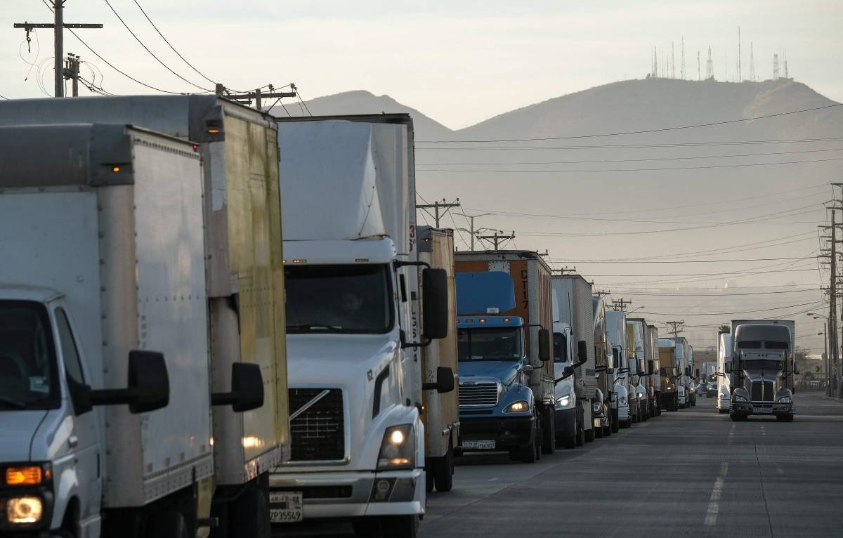 Trucks wait on a queue to cross to the US next to the border wall at the Otay commercial crossing port in Tijuana, Baja California state, Mexico on November 26, 2024. US President-elect Trump said Monday he would impose a 25 percent tariff on all imports from Mexico and Canada as one of his first actions upon becoming US president in January. (Photo by Guillermo Arias / AFP)