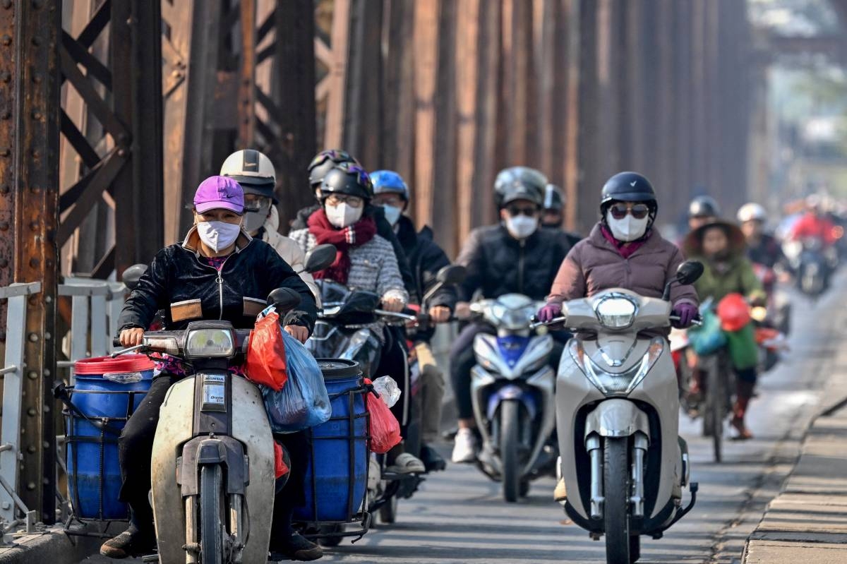 Motorists wearing face masks ride scooters along Long Bien Bridge amid heavy air pollution in Hanoi on January 3, 2025. - Thick smog blanketed Hanoi on January 3, obscuring buildings and leaving nine million residents choking on toxic air as the Vietnamese capital topped a list of the world's most polluted major cities. (Photo by Nhac NGUYEN / AFP)